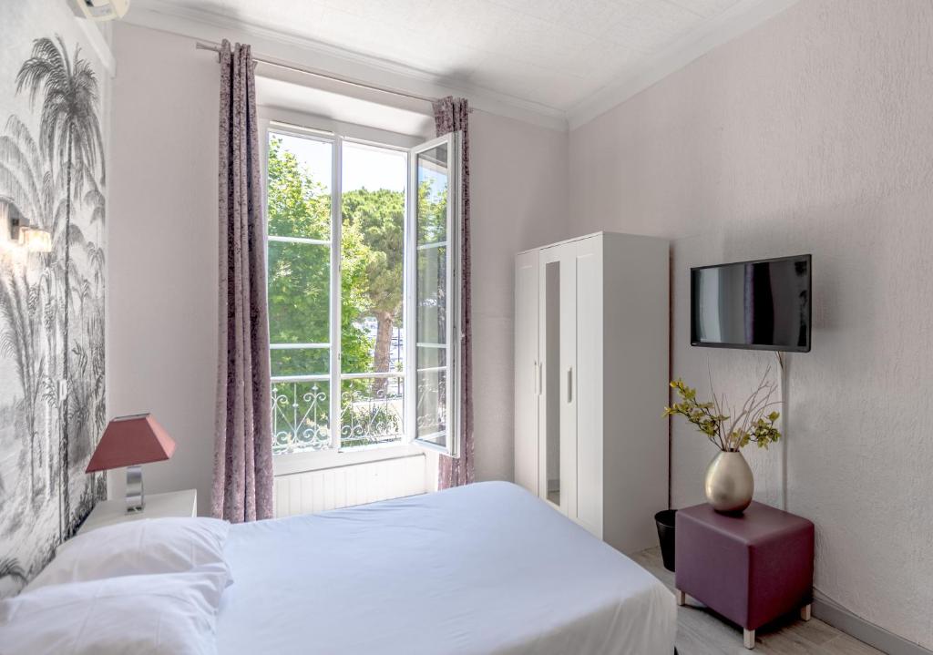 a white bedroom with a bed and a window at Hotel Les Palmiers in Sainte-Maxime
