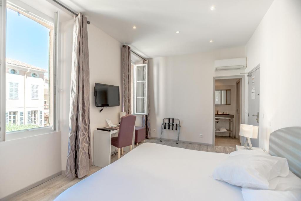a white bedroom with a bed and a desk and a window at Hotel Les Palmiers in Sainte-Maxime