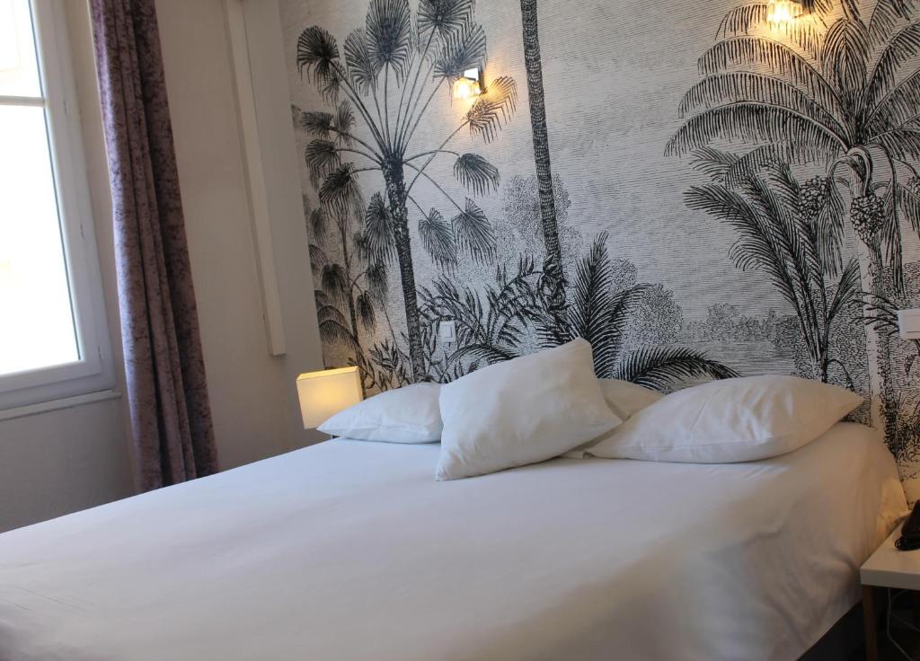 a bedroom with a bed with white sheets and palm wallpaper at Hotel Les Palmiers in Sainte-Maxime