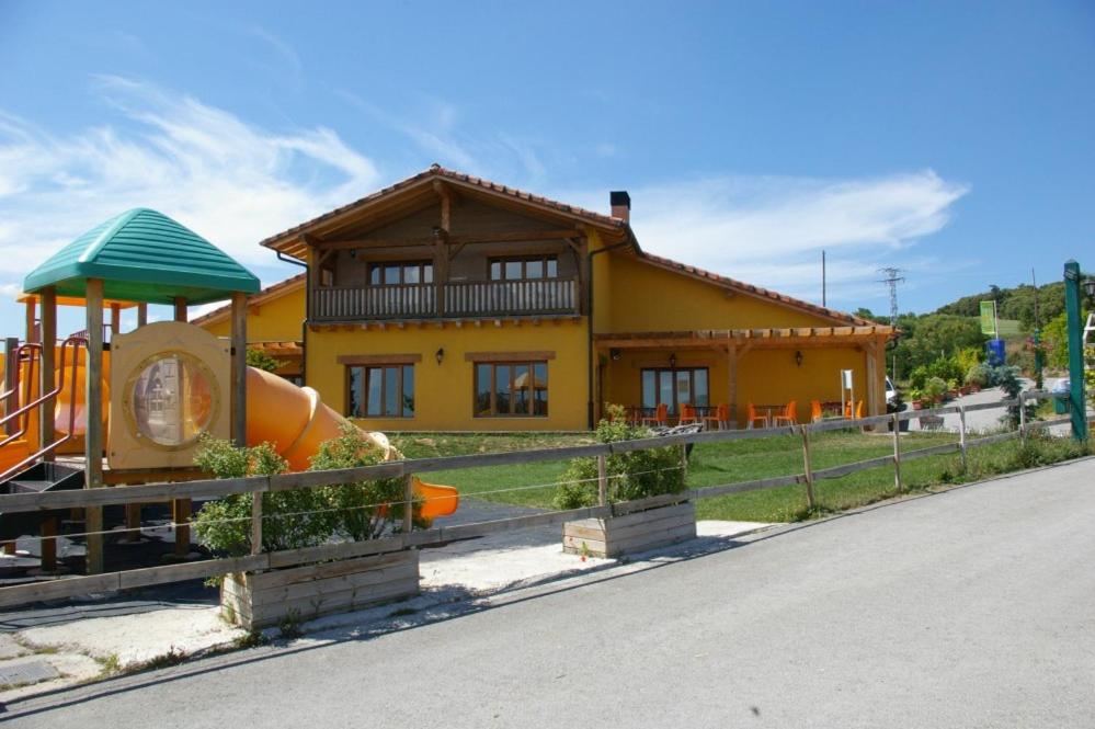 una casa amarilla con un patio de juegos delante de ella en Camping El Roble Verde, 