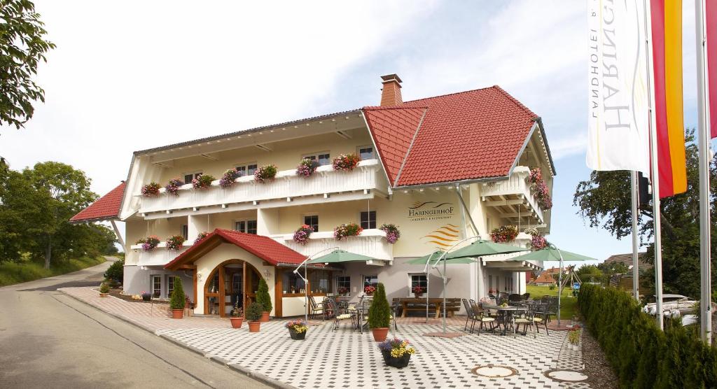 ein Gebäude mit einem roten Dach und einer Terrasse in der Unterkunft Landhotel Haringerhof mit Saunawelt und Naturbadeteich in Grafenhausen