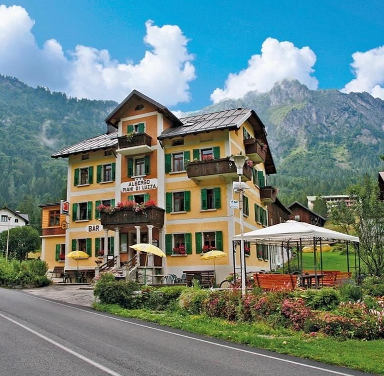 un grand bâtiment sur le côté d'une route dans l'établissement Albergo Piani di Luzza, à Forni Avoltri