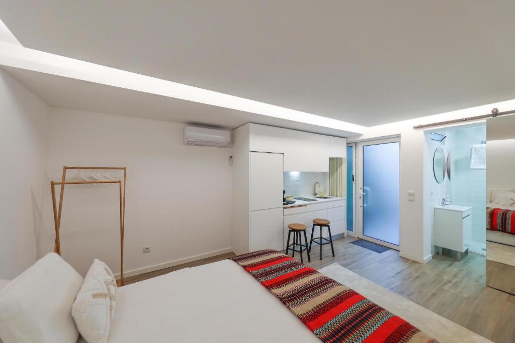 a white bedroom with a bed and a kitchen at Estúdio Cândida, One place … in Nazaré