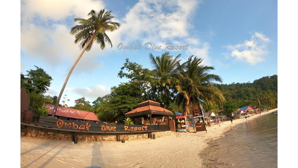 a beach with a restaurant and a palm tree at Ombak Dive Resort Perhentian Island in Perhentian Island