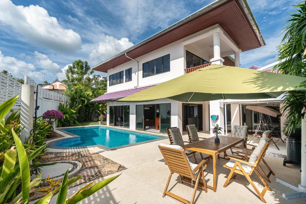 a villa with a swimming pool and a table with a green umbrella at Villa Amaya, 2 Story Tropical Oasis with Green Hills View & Pool, Kamala Beach in Kamala Beach