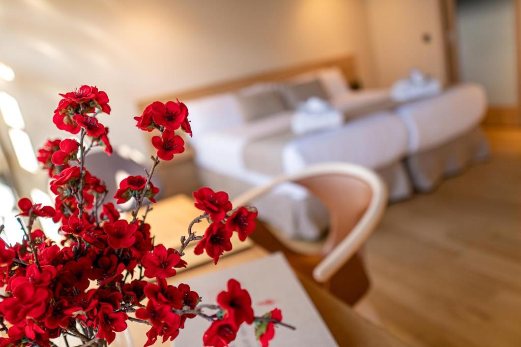 ACOUGA Hotel Boutique في ثيلانوفا: مزهرية مع الزهور الحمراء على طاولة في غرفة النوم