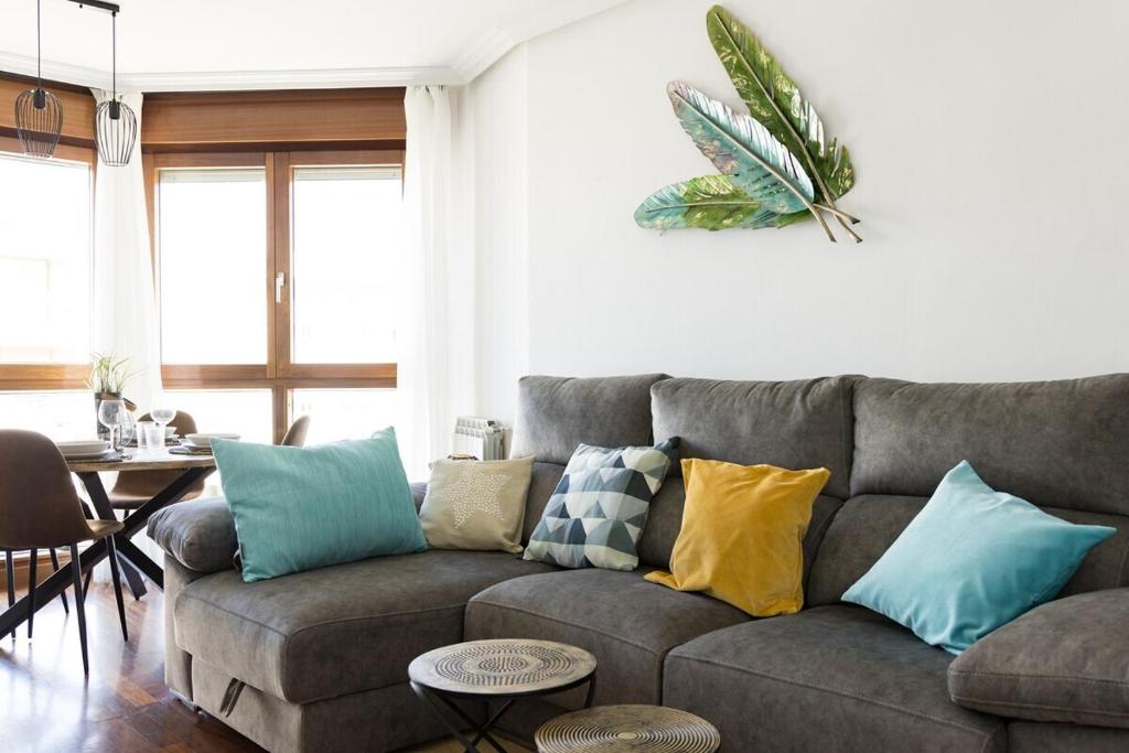 ein Wohnzimmer mit einem grauen Sofa und bunten Kissen in der Unterkunft MyHouseSpain - Playa de poniente, con vistas al mar y parking gratuito in Gijón