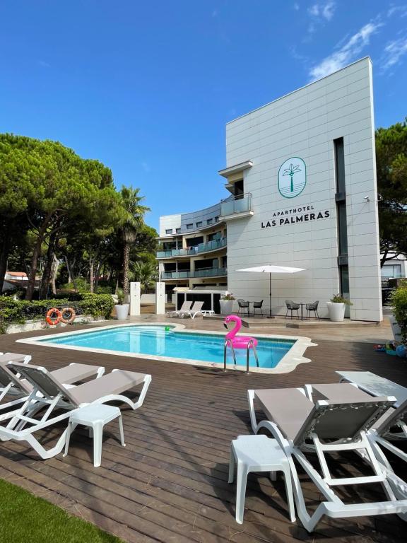 Aparthotel Las Palmeras Castelldefels في كاستيلديفِيلس: مسبح وكراسي وفطائر وردية بجوار مبنى