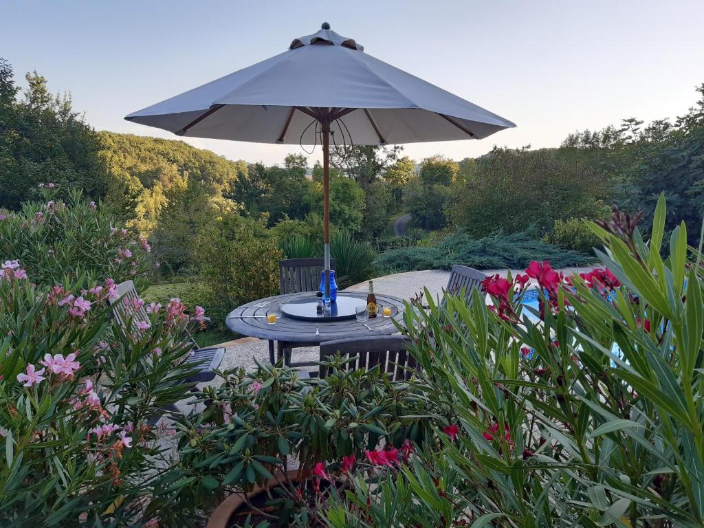 - une table avec un parasol dans un jardin fleuri dans l'établissement Gîte appartement, Sous les Arbres, à Montagudet