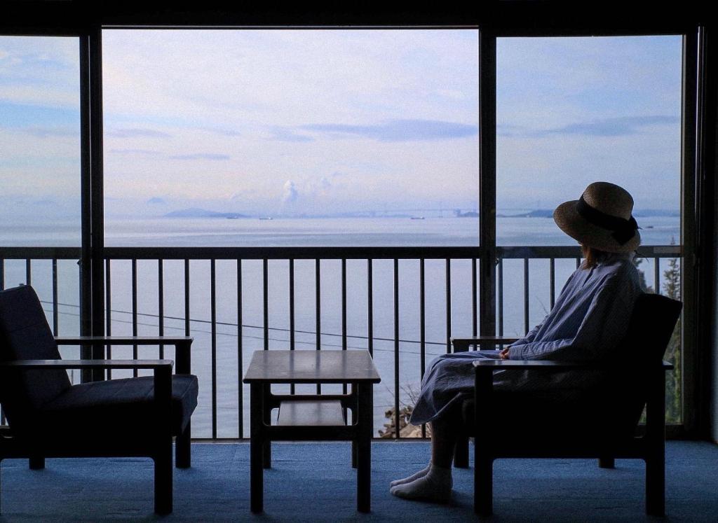 Eine Frau auf einem Stuhl mit Blick auf den Ozean in der Unterkunft DENIM HOSTEL float in Kurashiki