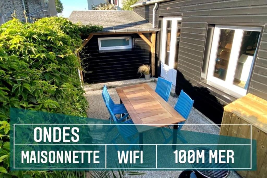 un pequeño patio trasero con mesa de madera y sillas en Maisonnette,100m mer, proche St Malo/Cancale, WIFI, en Saint-Benoît-des-Ondes