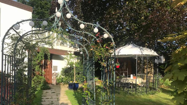 un jardín con un arco con una mesa y una sombrilla en Ferienzimmer Rogi, en Reinhardshausen