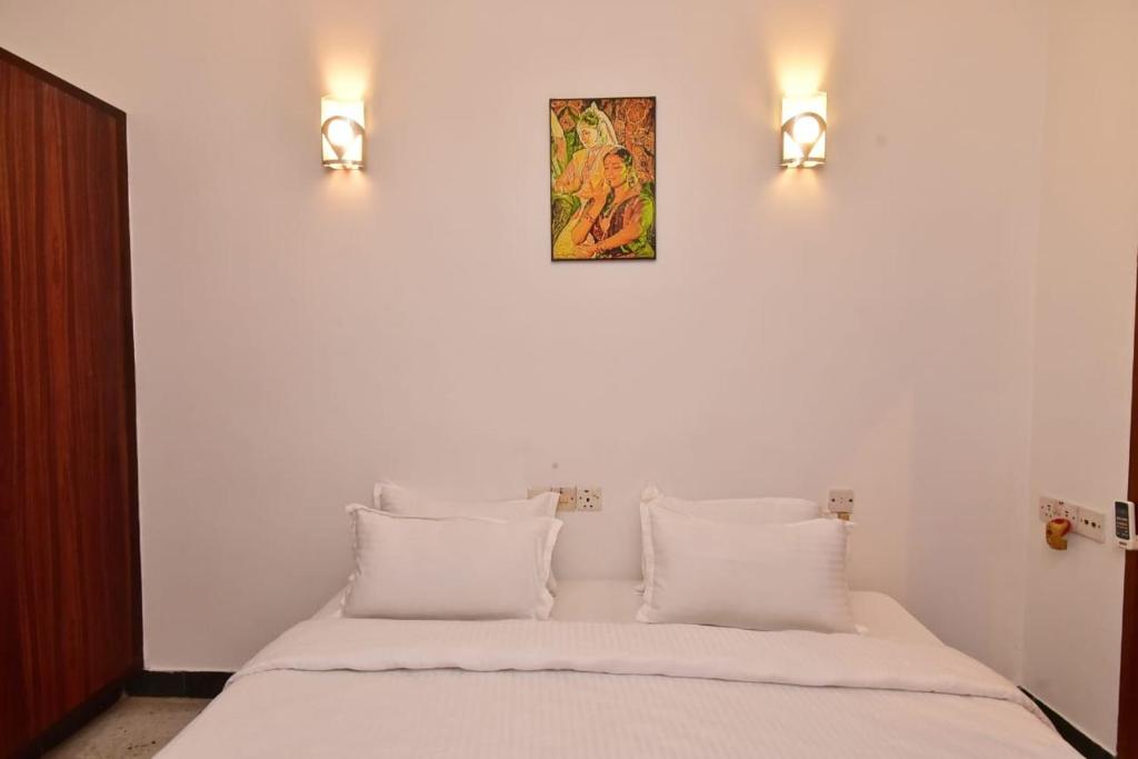 1 cama con almohadas blancas y 2 luces en la pared en Villa Felicia en Pondicherry