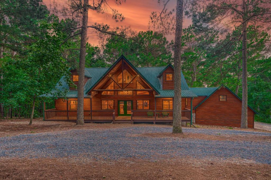 a log cabin in the woods with a sunset at The Eastwood Spacious Retreat with 4 King En-Suites - Hot Tub - Pet-Friendly - Cozy Fire Pit - Prime Location - Multi-Family in Broken Bow