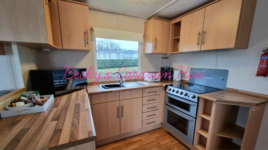 cocina con armarios de madera, fregadero y ventana en Becky's Caravan at Marton Mere, en Blackpool