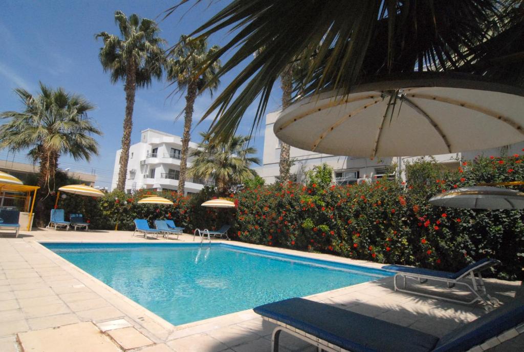 una piscina con sombrilla y palmeras y un edificio en Sunflower Hotel Apartments en Lárnaca