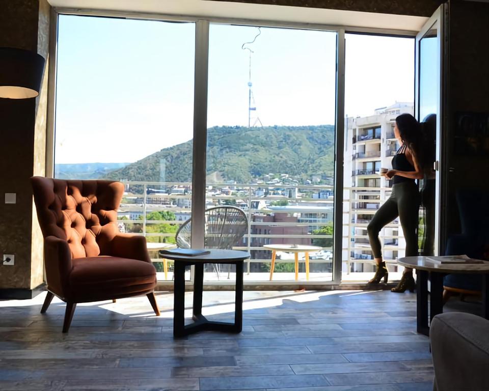 Eine Frau steht in einem Zimmer mit einem großen Fenster in der Unterkunft Panorama 360° Hotel in Tbilisi City