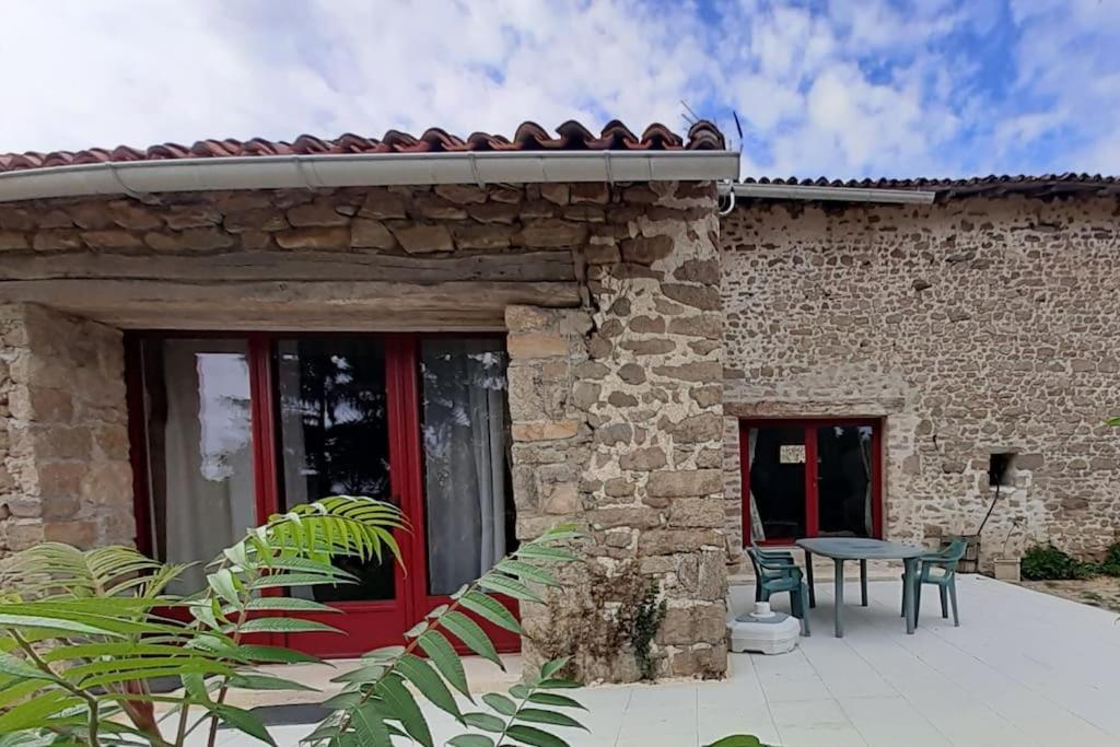 een stenen huis met een rode deur en een tafel bij Gîte de la Grange in Saint-Pardoux