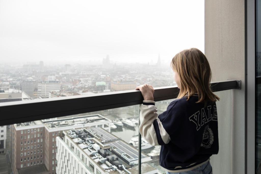 uma mulher a olhar pela janela para uma cidade em UNIEK appartement - mooiste en hoogste uitzicht op Antwerpen! - incl gratis parking em Antuérpia