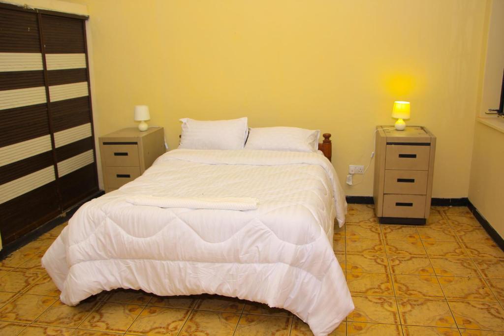 ein Schlafzimmer mit einem weißen Bett und zwei Nachttischen in der Unterkunft Namishukwe House in Mongu