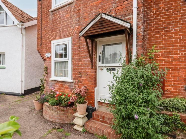 una casa de ladrillo con una puerta blanca y algunas plantas en The Pepper Pot en Lympstone