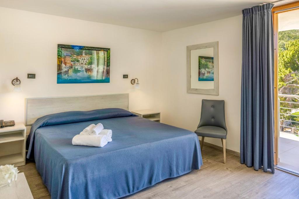a bedroom with a blue bed with a chair and a window at Pugnochiuso Resort Hotel del Faro in Vieste