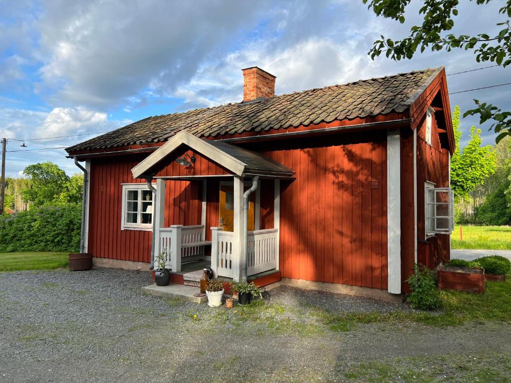 uma pequena casa vermelha com um alpendre branco em Lilla Backstugan em Nora