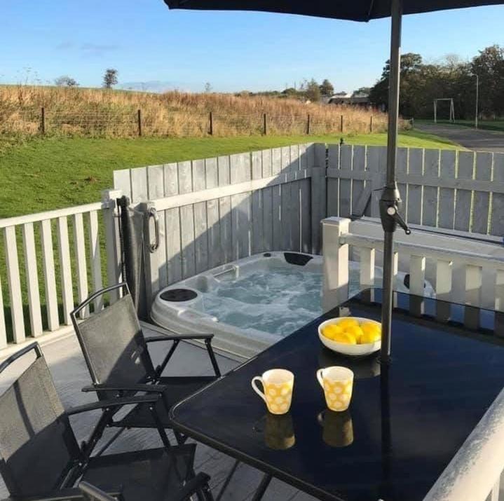 a patio table with an umbrella and a hot tub at Lemon Tree Lodge in Morpeth