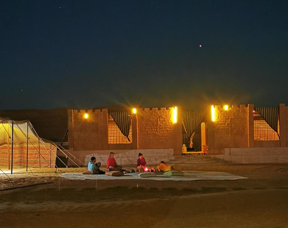 un groupe de personnes assises à terre la nuit dans l'établissement Desert Wonders Camp, à Ḩawīyah