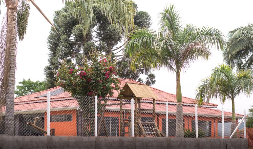um edifício laranja com palmeiras e uma cerca em Chácara Recanto da Paz em Pinhalzinho