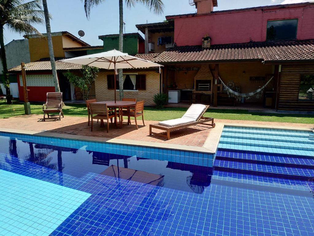 une piscine avec une table et des chaises ainsi qu'une maison dans l'établissement Flat Vila Caiçara, à Ilhabela