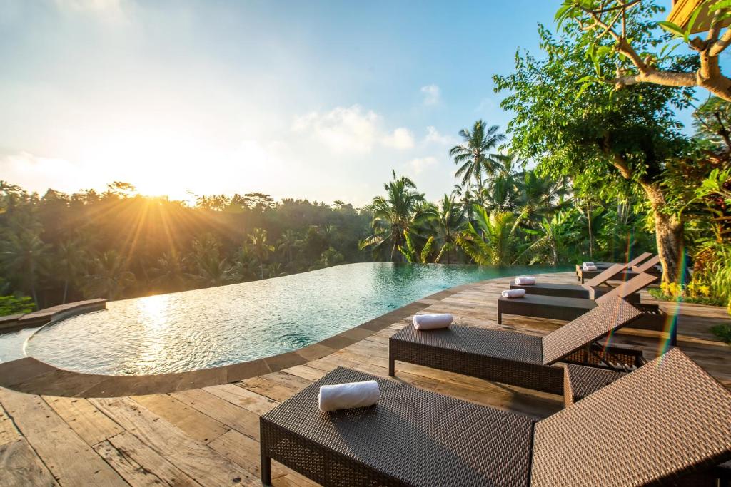 a pool at a resort with chairs and the sun setting at GK Bali Resort in Tegalalang
