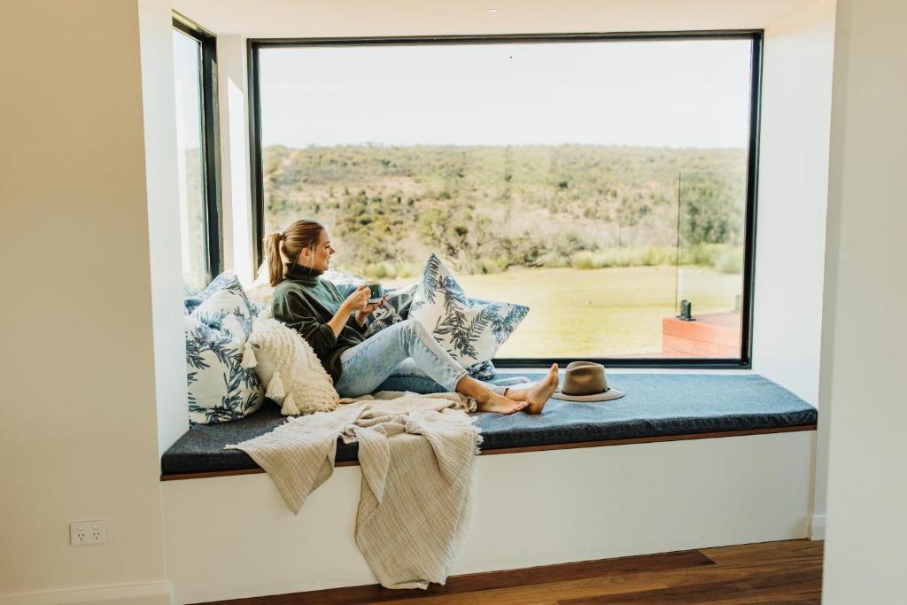 Eine Frau, die auf einem Fenstersitz sitzt und aus dem Fenster schaut. in der Unterkunft StowAway Kangaroo Island in Stokes Bay