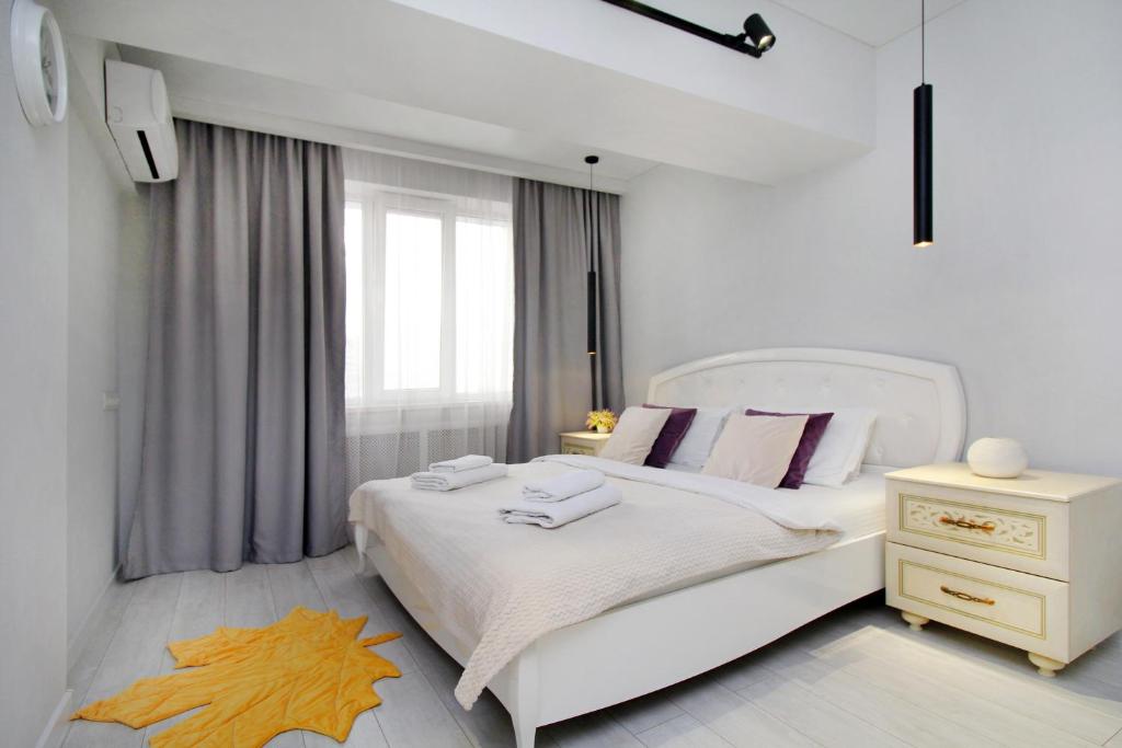 1 dormitorio blanco con 1 cama blanca grande con almohadas rosas en уютная квартира-студия в центре Алматы, en Almaty