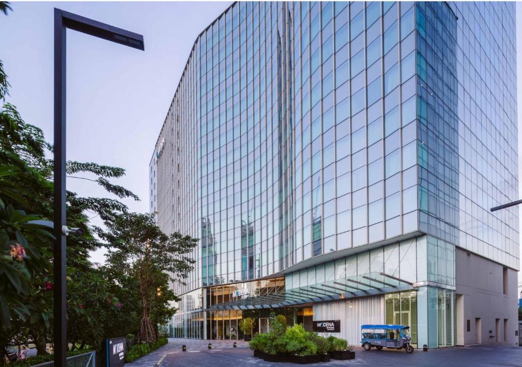 a tall glass building with a blue truck in front of it at Modena by Fraser Bangkok in Bangkok