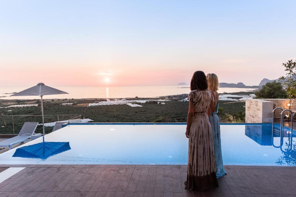 a woman standing by a swimming pool looking at the sunset at Falasarna Luxury Villas in Falasarna