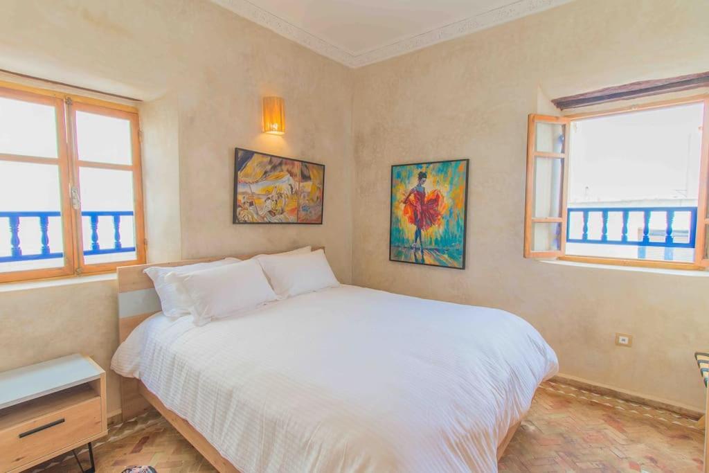 a bedroom with a white bed and two windows at Stella 3 - superbe appartement avec cheminée en médina in Essaouira