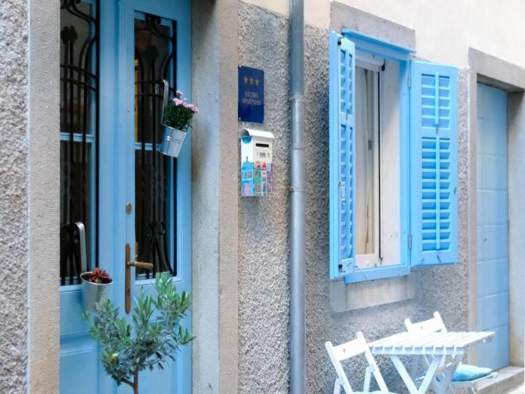 ein Gebäude mit blauen Fensterläden, einem Tisch und einem Stuhl in der Unterkunft Apartments Blue Lavender in Cres