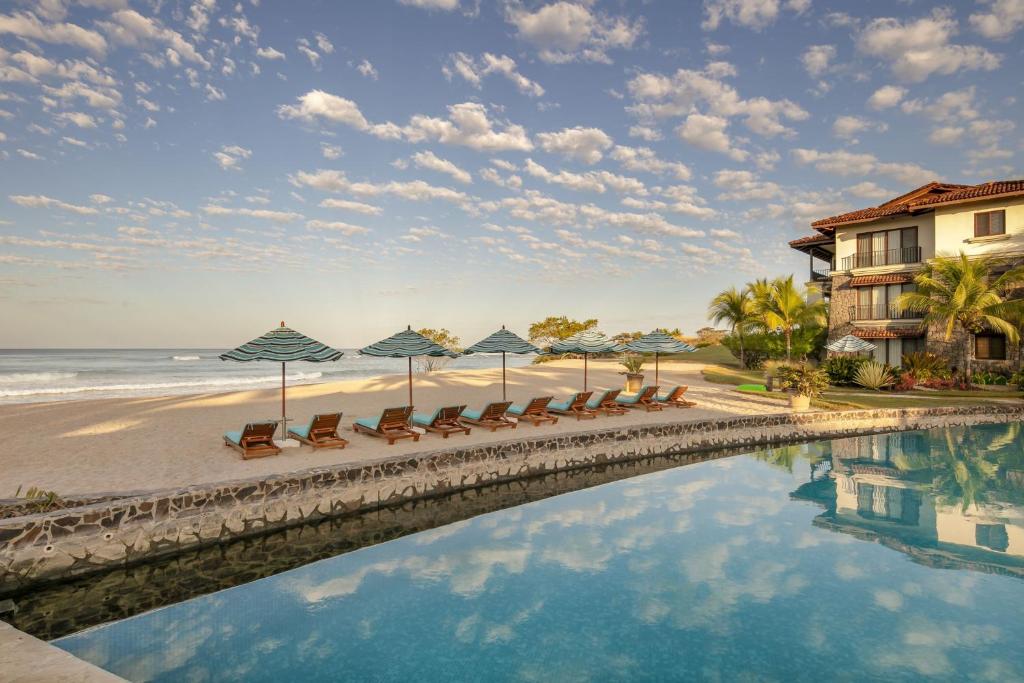 una piscina en la playa con sillas y sombrillas en JW Marriott Guanacaste Resort & Spa en Tamarindo