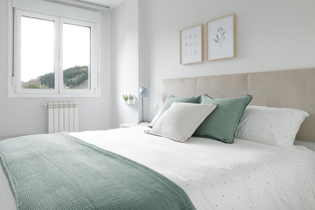 a white bedroom with a bed with green and white pillows at Apartamentos Nature in Cangas del Narcea