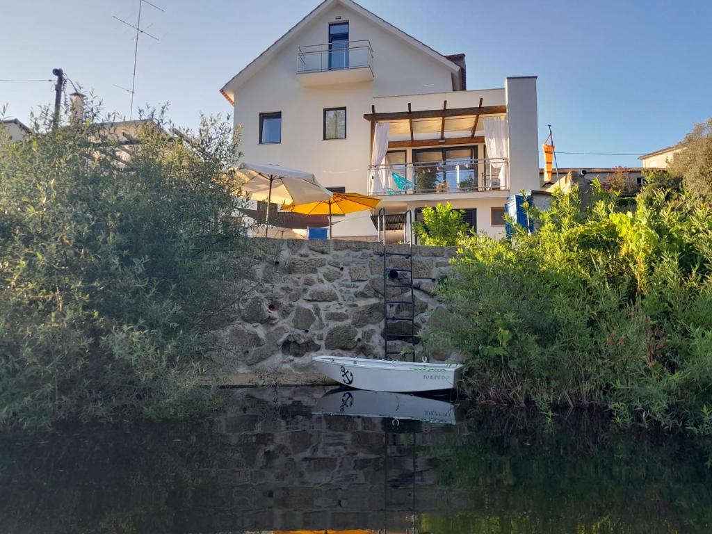 a house with a boat in a body of water at Ínsua Hostel in São Pedro do Sul