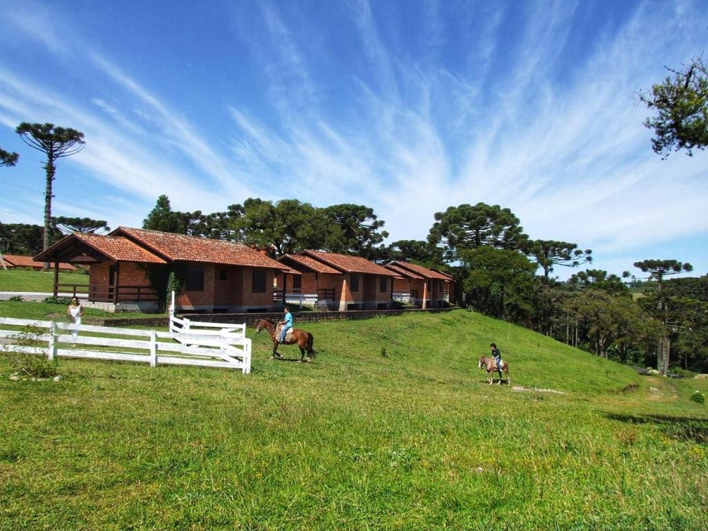 two people riding horses in a field next to a house at Morada Das Araucárias in São Francisco de Paula