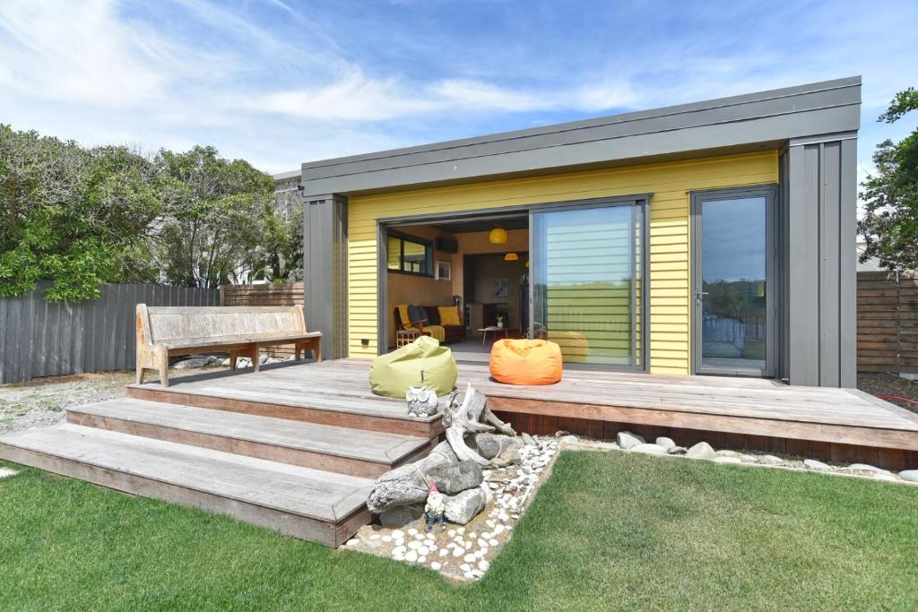 einen Hinterhof mit einer Holzterrasse und einem Haus in der Unterkunft Beachfront Bach - Christchurch Holiday Homes in Christchurch