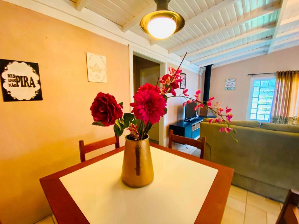 un jarrón con flores rojas sobre una mesa en la sala de estar en Nena's House - Banheira de Hidromassagem-10 Pessoas, en Gramado