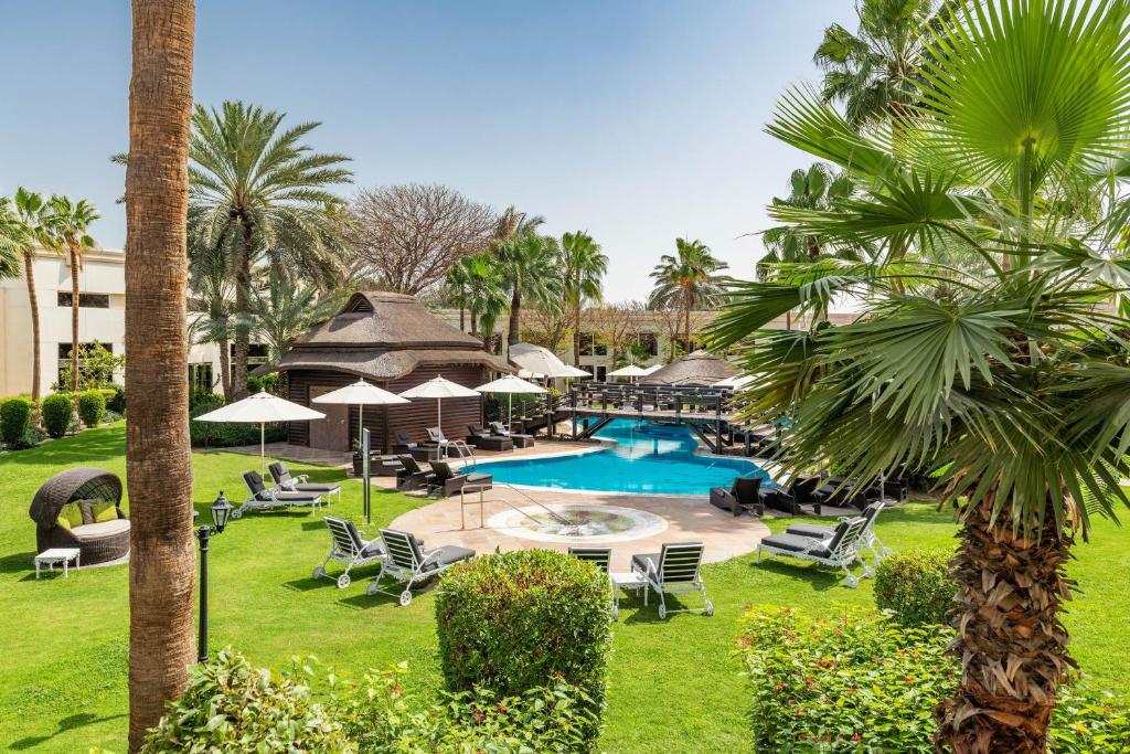 a resort with a pool and chairs and palm trees at Le Méridien Dubai Hotel & Conference Centre in Dubai