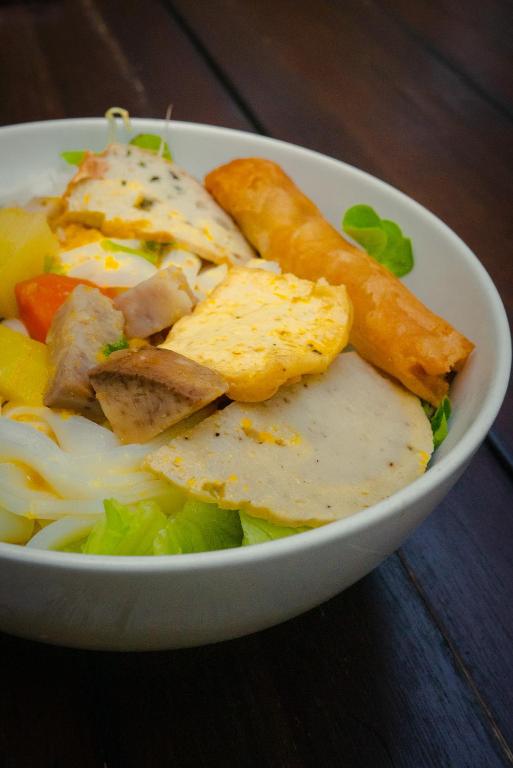A bowl of Vietnamese-style noodles topped with egg, meat, vegetables, and a spring roll.