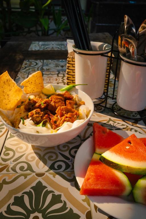 A noodle dish served with watermelon and table utensils.