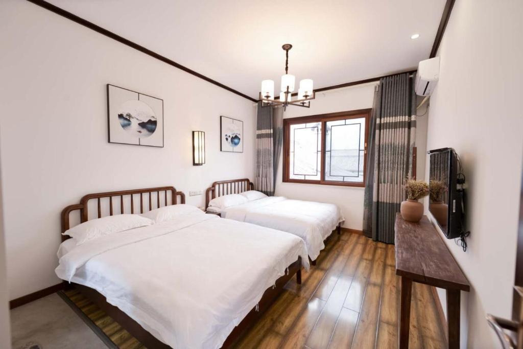 two beds in a bedroom with white walls and wood floors at Jiamen Inn in Emeishan City