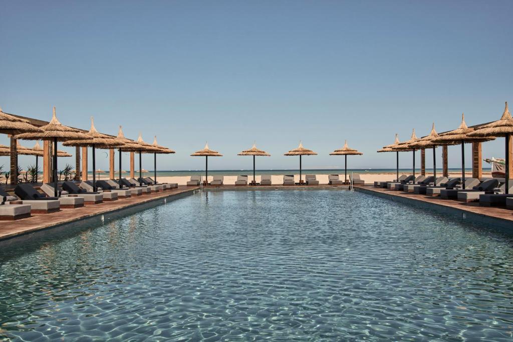 una piscina con sillas y sombrillas en la playa en Casa Cook El Gouna - Adults Only en Hurghada