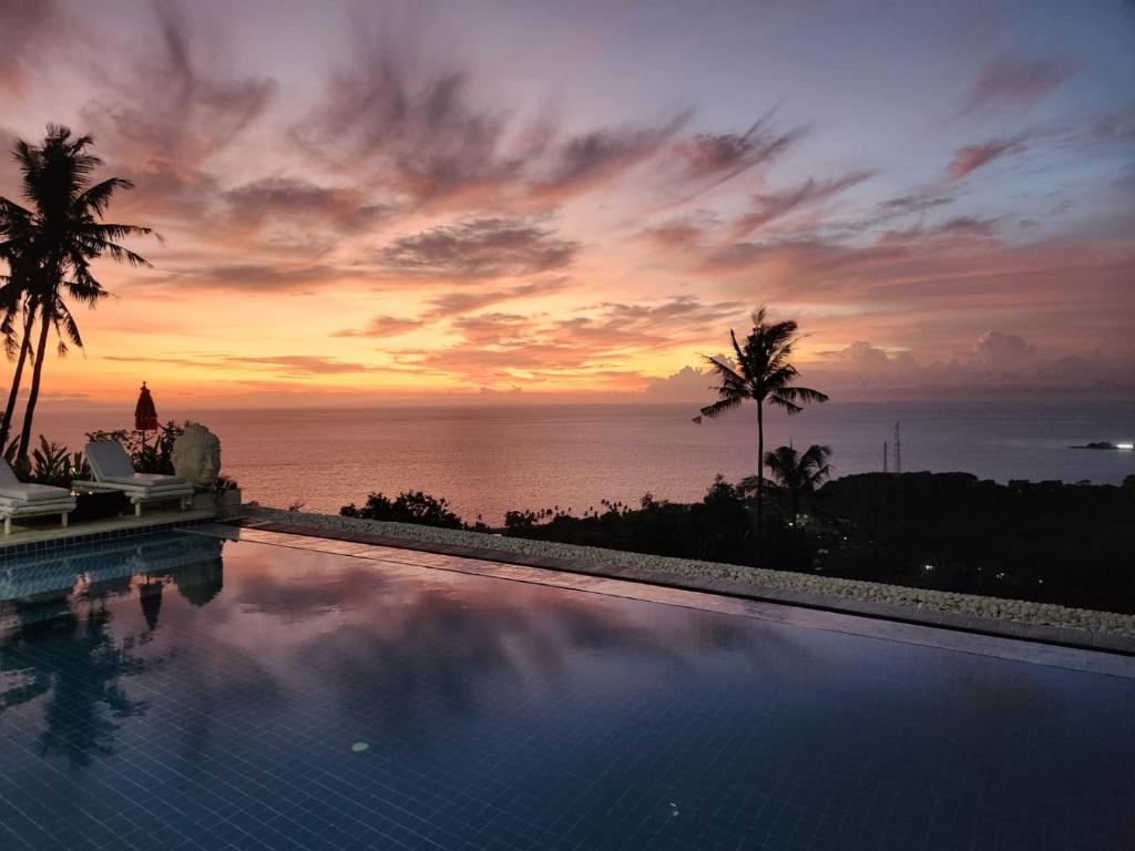a swimming pool with a sunset over the ocean at Villa Umbrella in Senggigi 